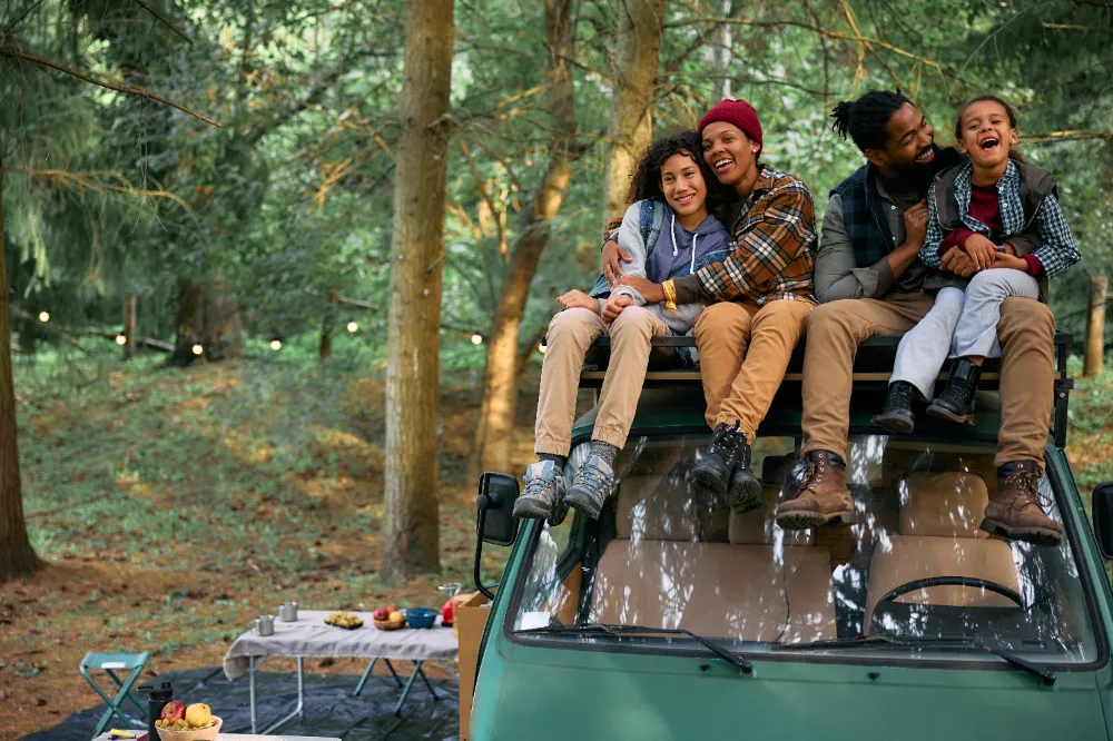 Cheerful African American family sitting on camper trailer in the woods